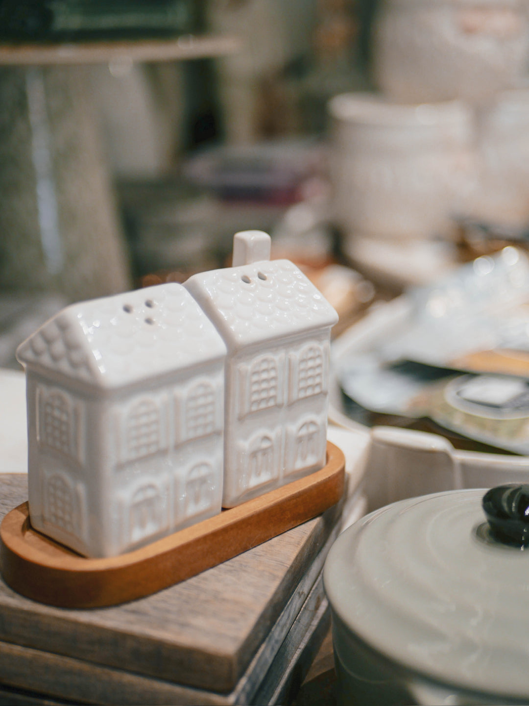 White ceramic salt and pepper shakers shaped like houses on a wooden stand.