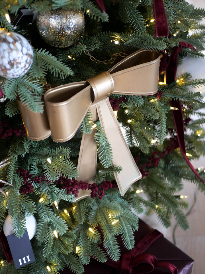 Decorative gold bow on a Christmas tree with lights and ornaments.