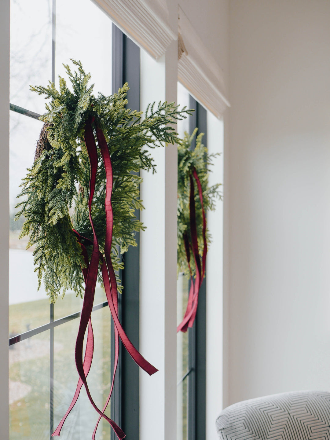Green wreaths with red ribbons hanging on a window