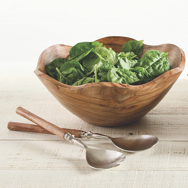 Wooden salad bowl with fresh spinach leaves on a light wooden surface with two spoons.