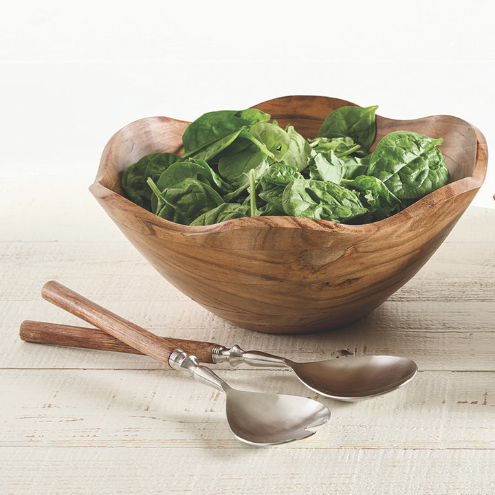 Wooden salad bowl with fresh spinach leaves on a light wooden surface with two spoons.