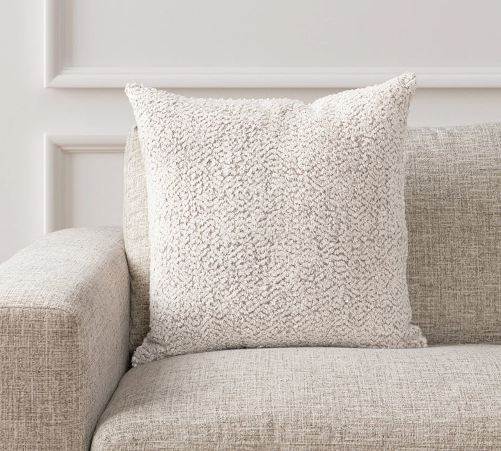 Textured beige pillow on a beige sofa against a white wall