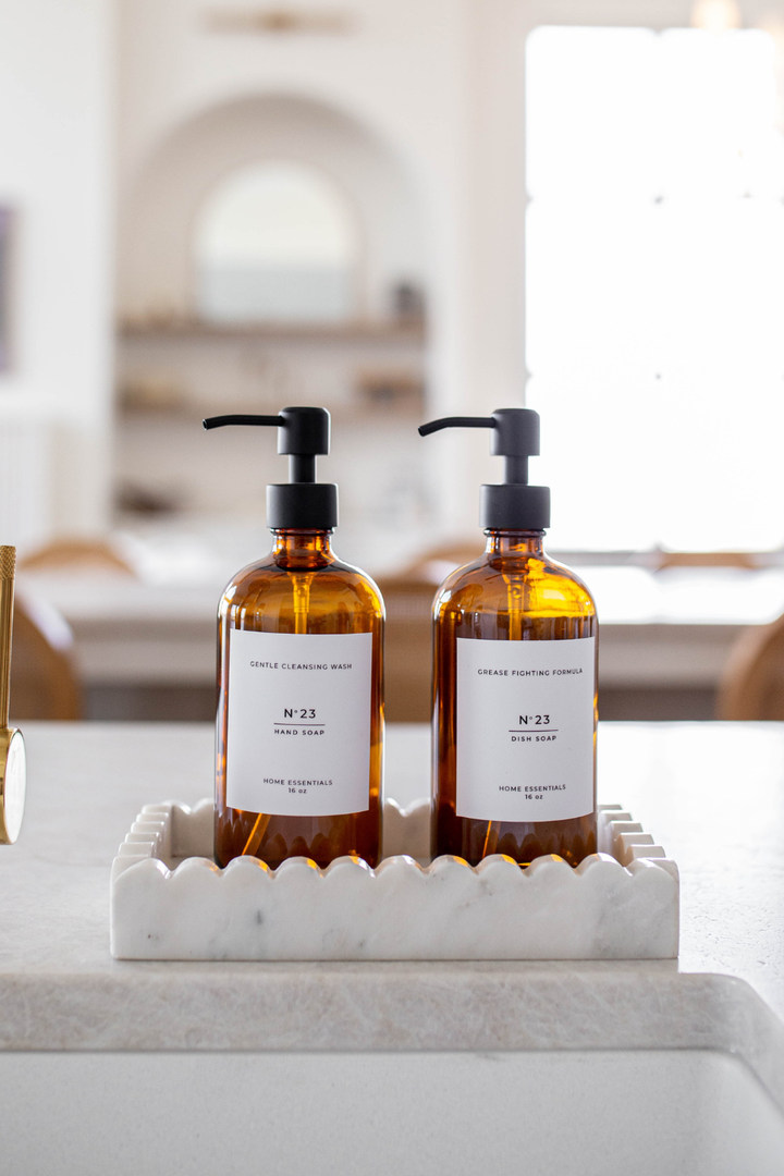 Two amber glass bottles with pump dispensers on a marble tray in a bathroom setting.