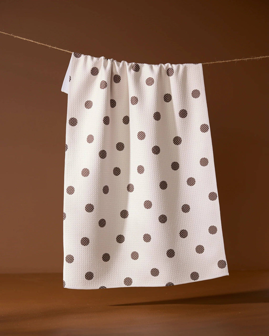 White towel with brown polka dots hanging on a line against a brown background