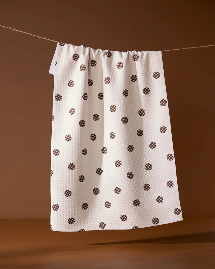 White towel with brown polka dots hanging on a line against a brown background