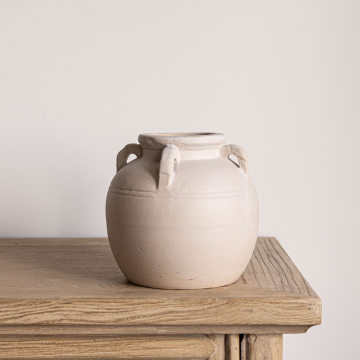 Beige ceramic vase with handles on a wooden surface against a plain background