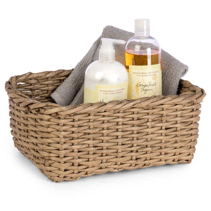 Bathroom essentials basket with two bottles of soap and a towel in a woven basket on a white background