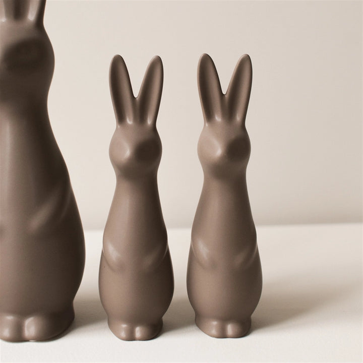 Three brown ceramic rabbit sculptures of varying sizes on a light background