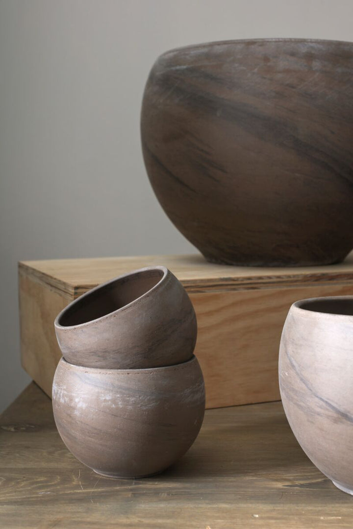 Three brown ceramic pots of varying sizes on a wooden surface with a neutral background