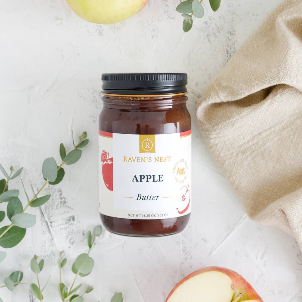 Jar of Raven's Nest Apple Butter on a light background with apples and leaves.