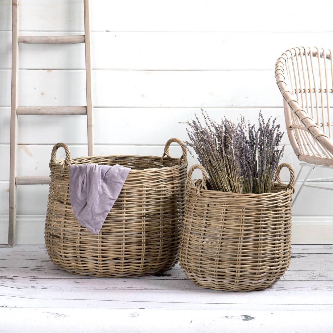 Two wicker baskets on a wooden floor with a white wall and chair in the background.