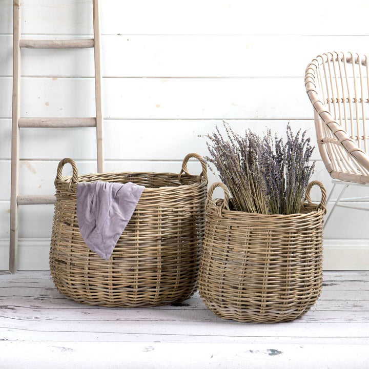 Two wicker baskets on a wooden floor with a white wall and chair in the background.