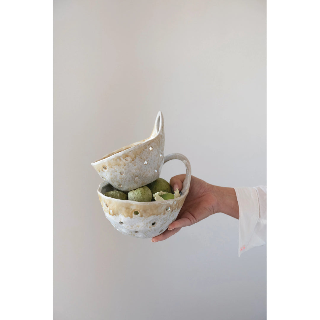 Hand holding a unique ceramic colander and bowl set with green stones inside on a plain background