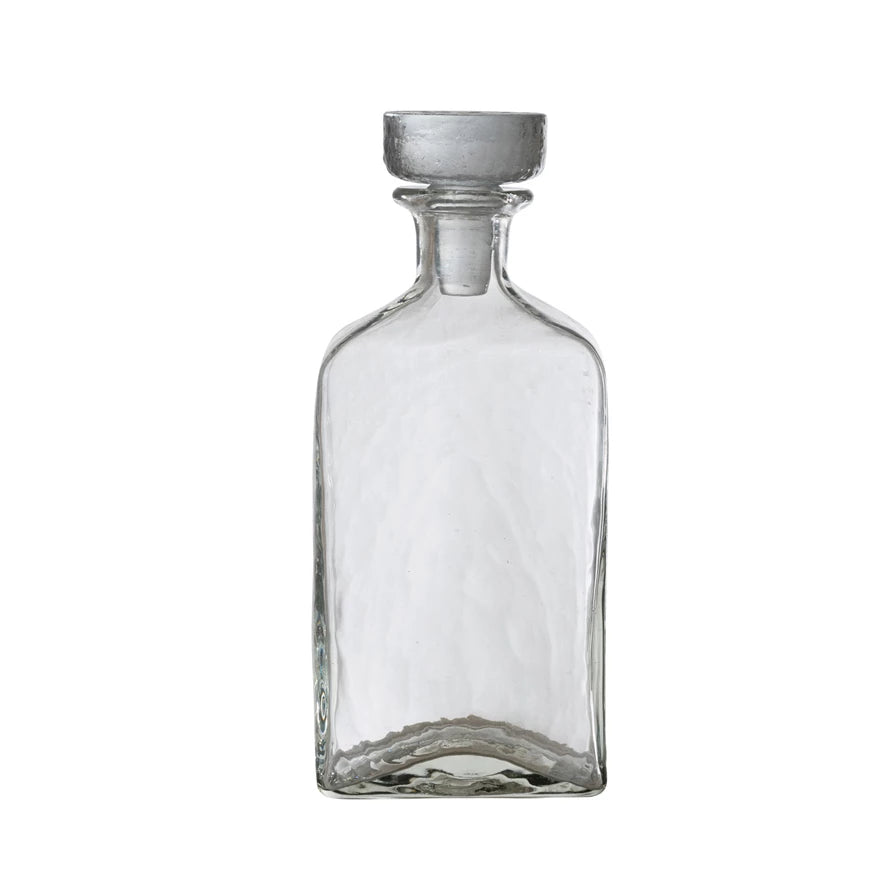 Clear glass decanter with a metallic cap on a white background