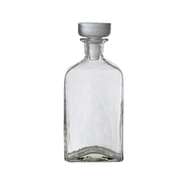 Clear glass decanter with a metallic cap on a white background