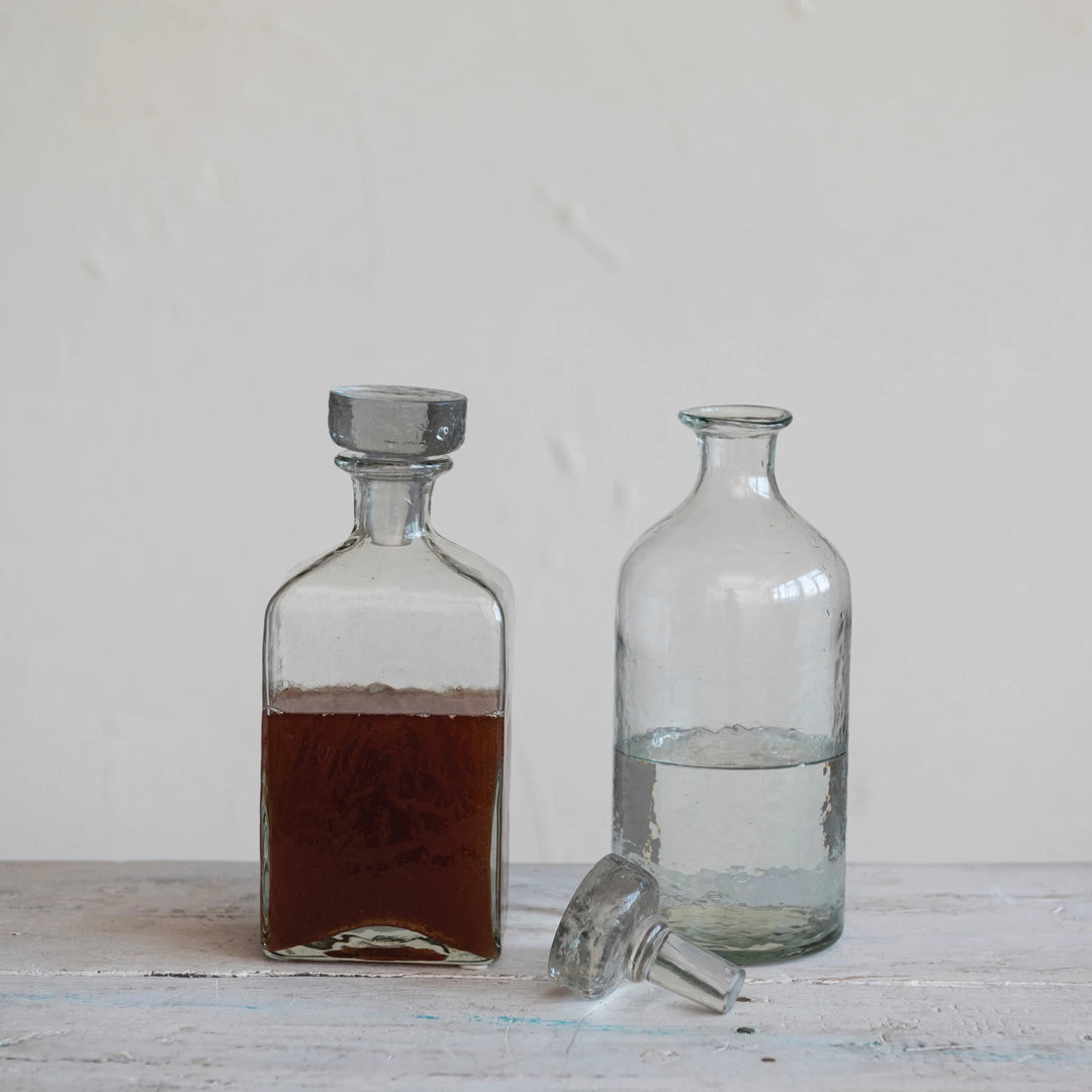 Two glass decanters, one with a dark liquid and the other with clear liquid, on a wooden surface.