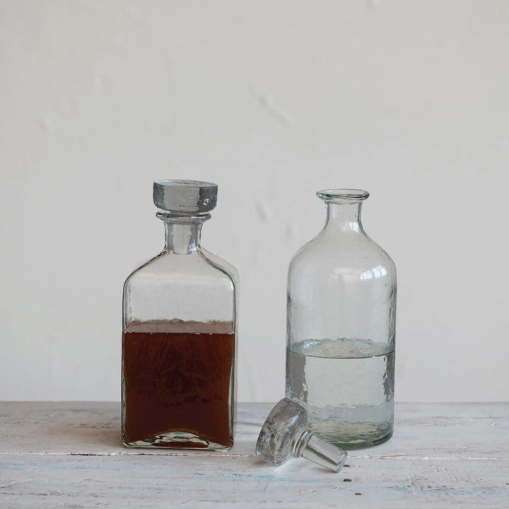 Two glass decanters, one with a dark liquid and the other with clear liquid, on a wooden surface.