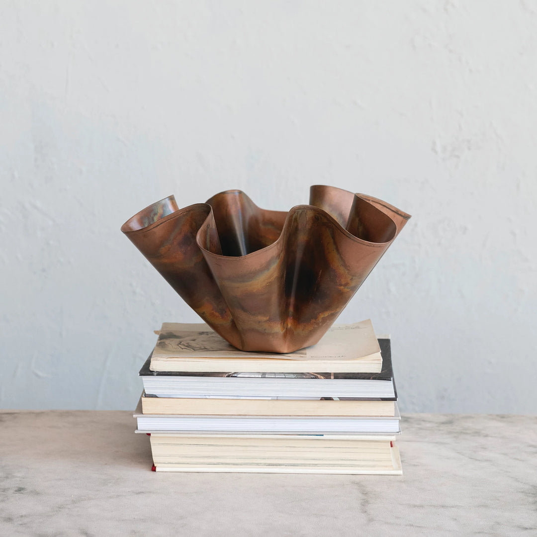 Copper vase on a stack of books against a plain background