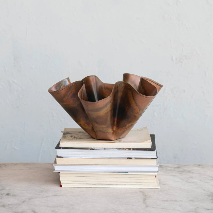 Copper vase on a stack of books against a plain background