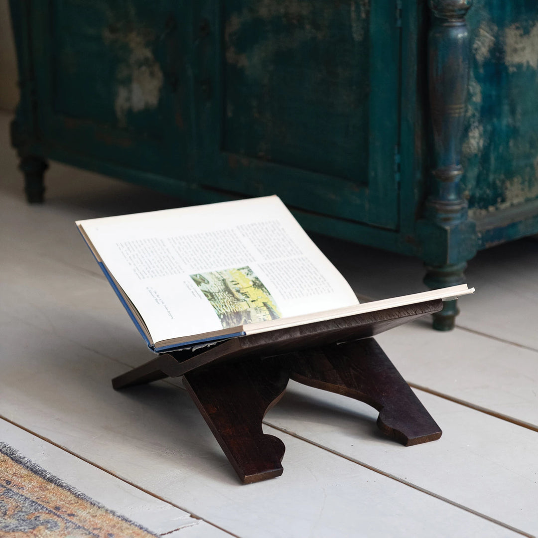 Open book on a wooden stand with a vintage cabinet in the background
