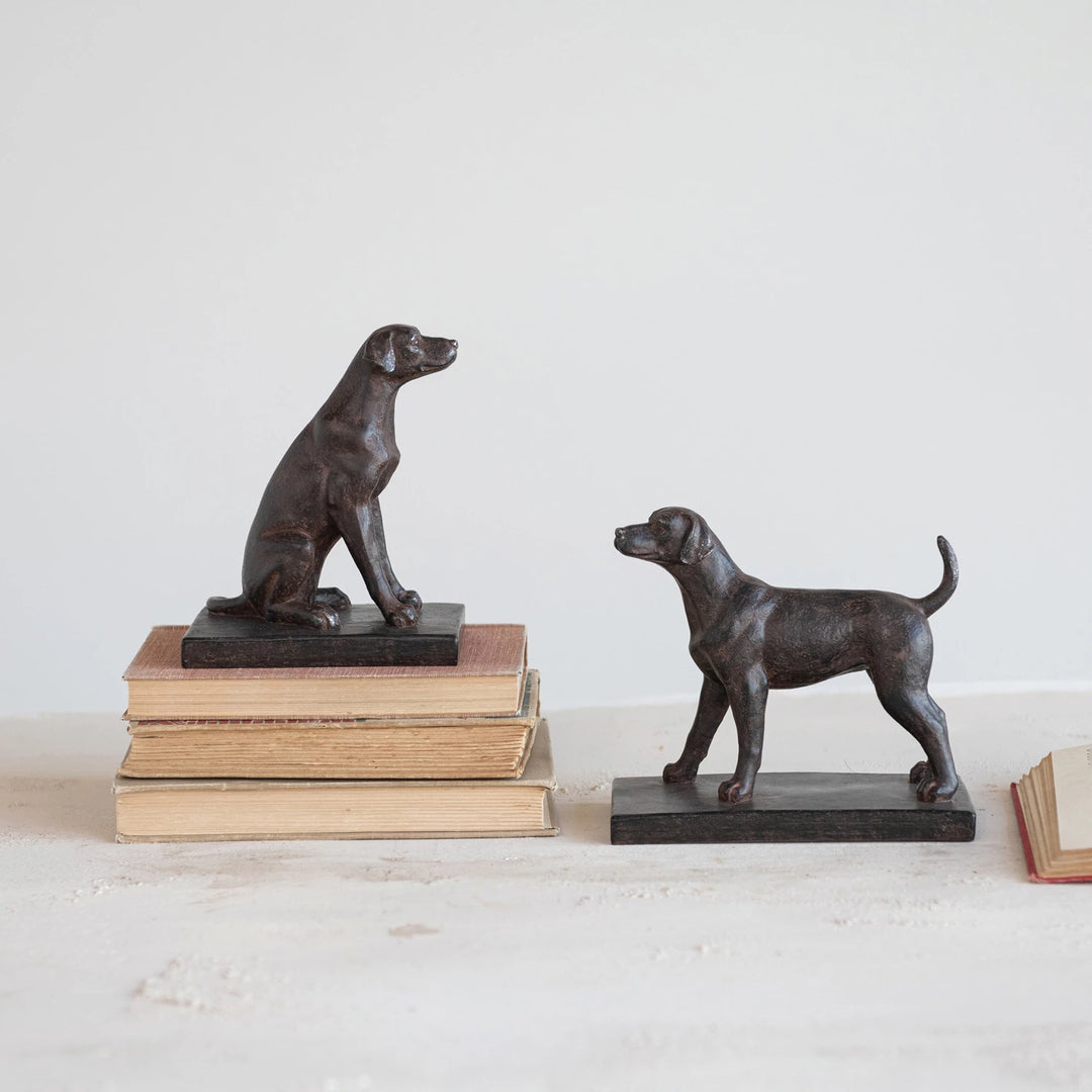 Two bronze dog sculptures on books against a white background