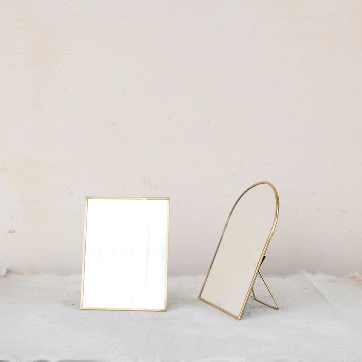 Two gold-framed mirrors on a white surface with a light gray background