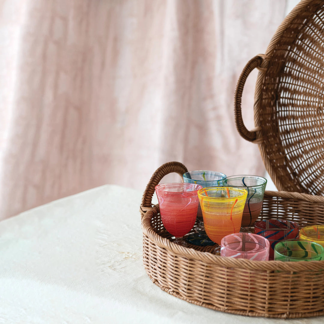 Colorful glassware in a wicker basket on a light surface with a soft pink curtain background