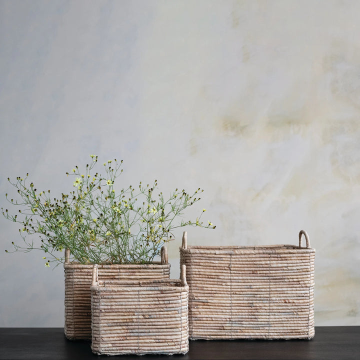Three woven baskets with plants against a plain wall