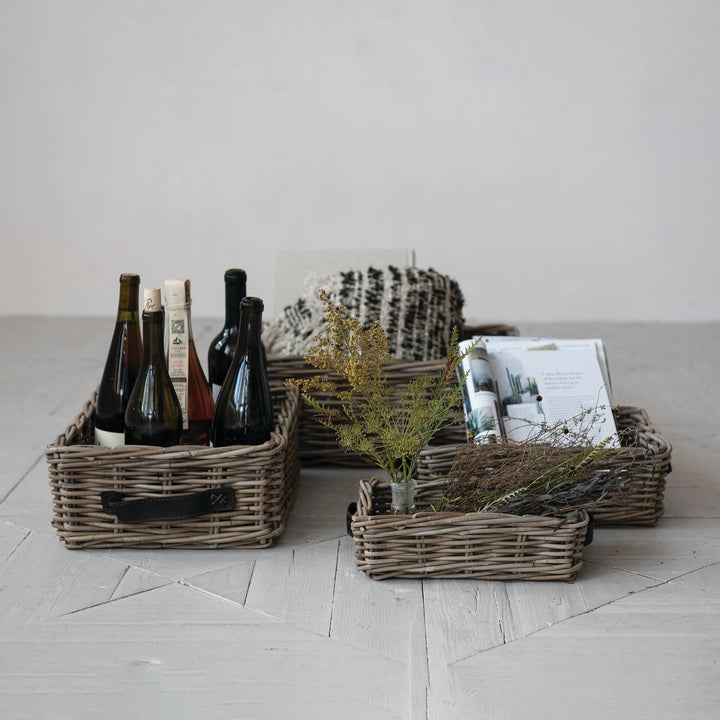 Wicker baskets with bottles, plants, and books on a light wooden floor.