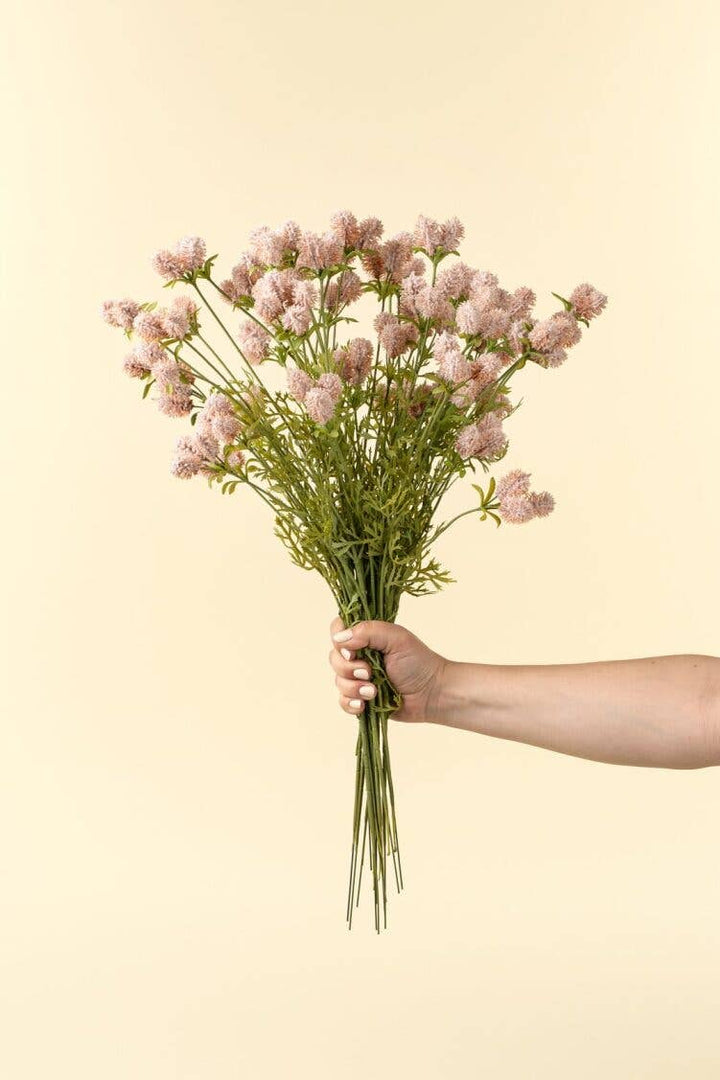 Hand holding a bouquet of pink flowers against a beige background