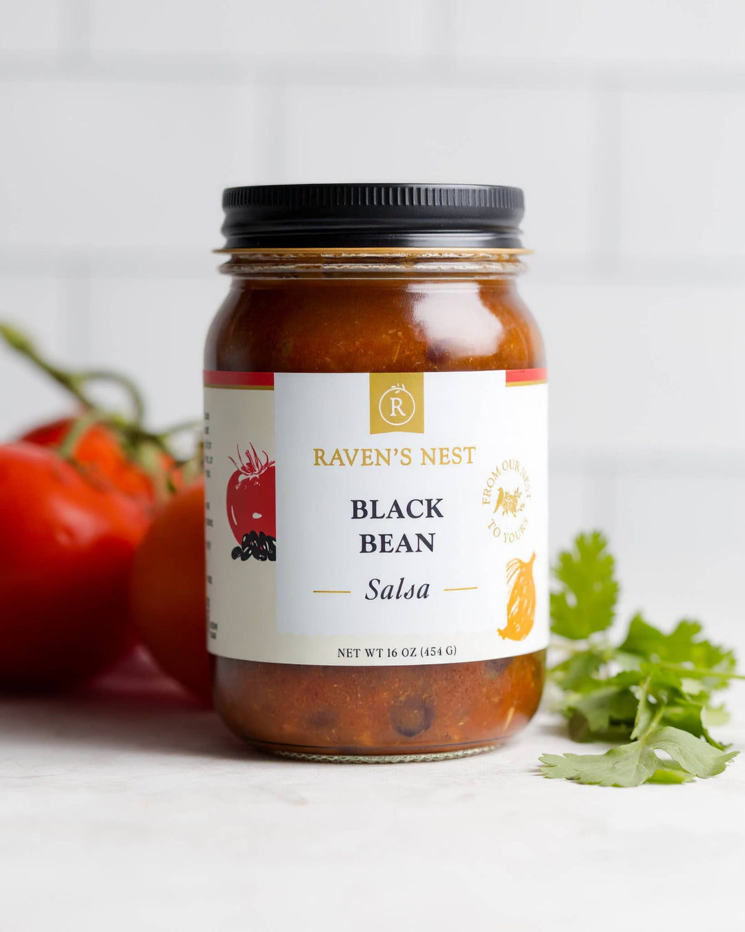 Jar of Raven's Nest Black Bean Salsa with tomatoes and cilantro on a white background