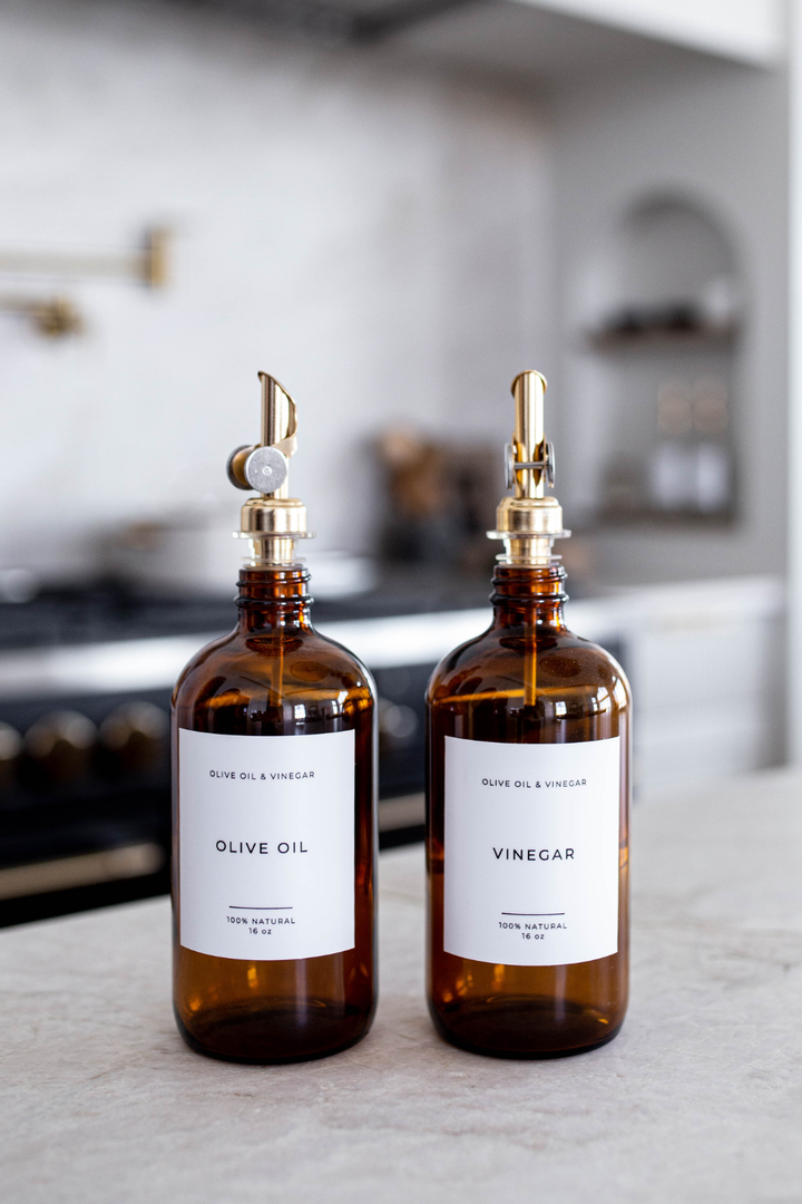 Two brown glass bottles labeled 'Olive Oil' and 'Vinegar' on a kitchen counter.