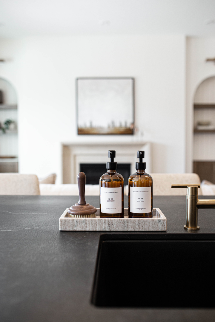 Two brown bottles with labels on a tray on a black countertop in a modern kitchen.