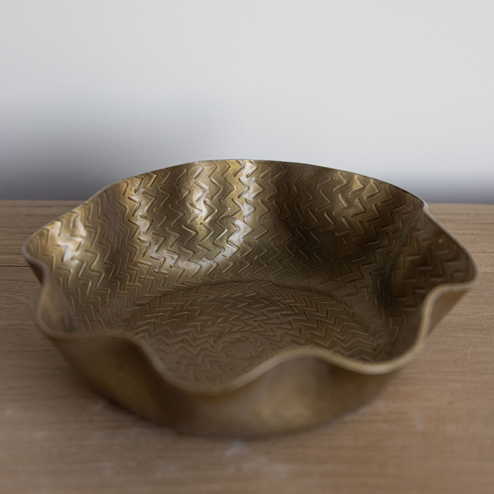 Bronze bowl with wavy edge and textured surface on a wooden surface