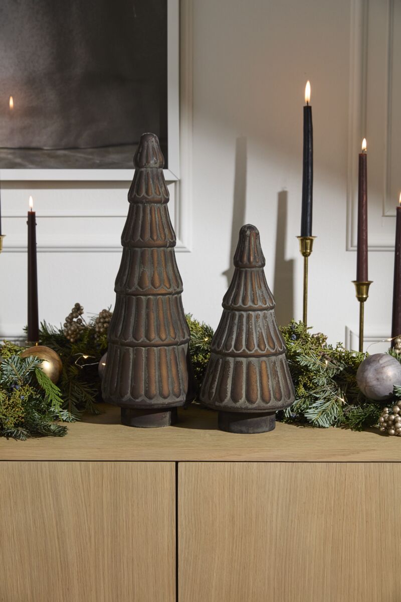 Two vintage bronze glass trees with a textured pattern, placed on a wooden surface with holiday decorations in the background, including candles and greenery.