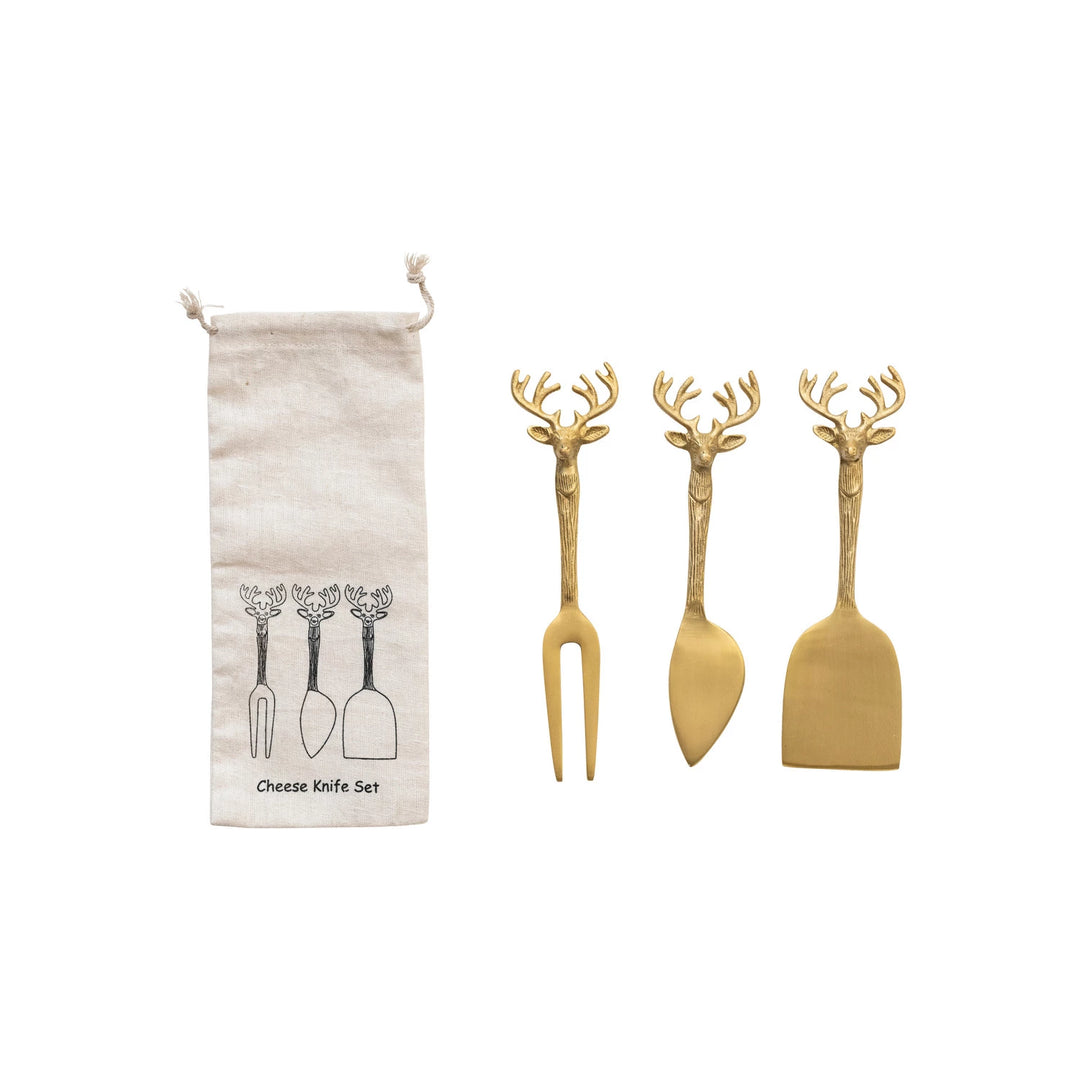 A set of three brass cheese knives with reindeer handles, displayed alongside a printed drawstring bag 