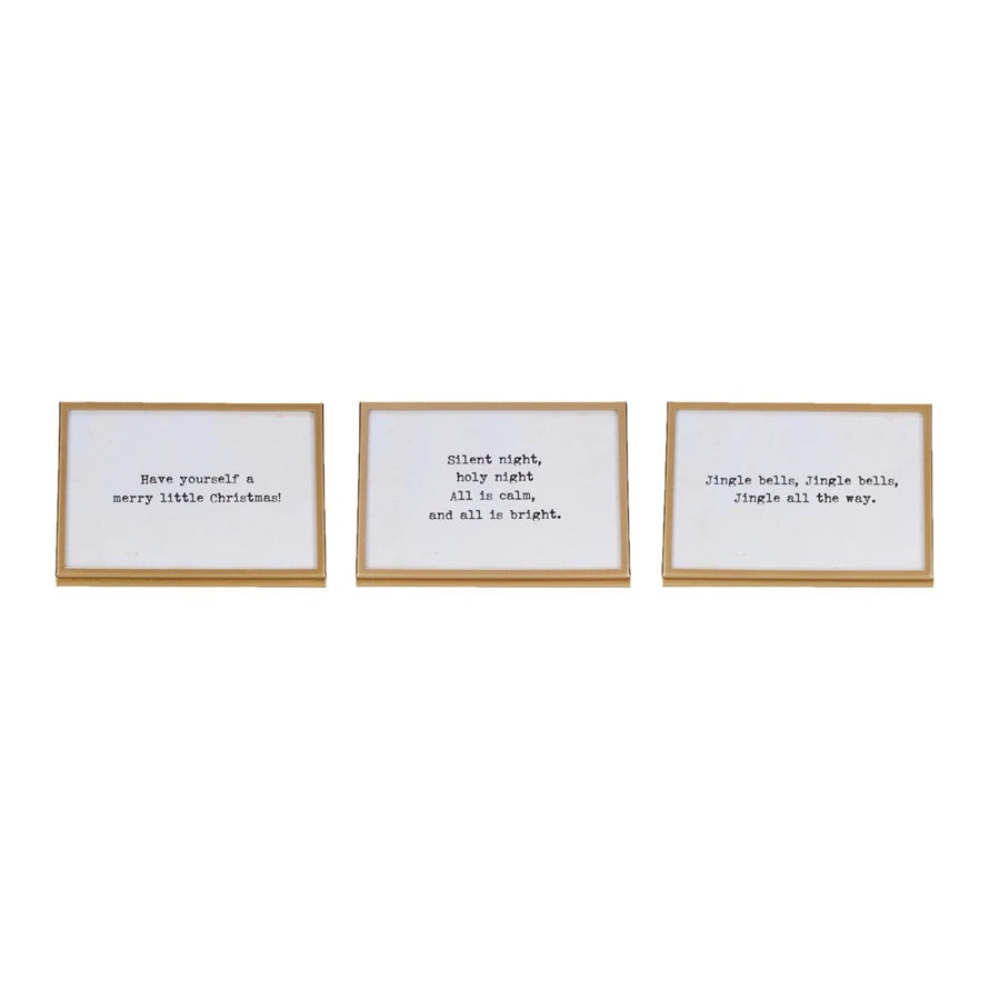 Three gold finish metal and glass frames with easels and Christmas-themed sayings written in them.